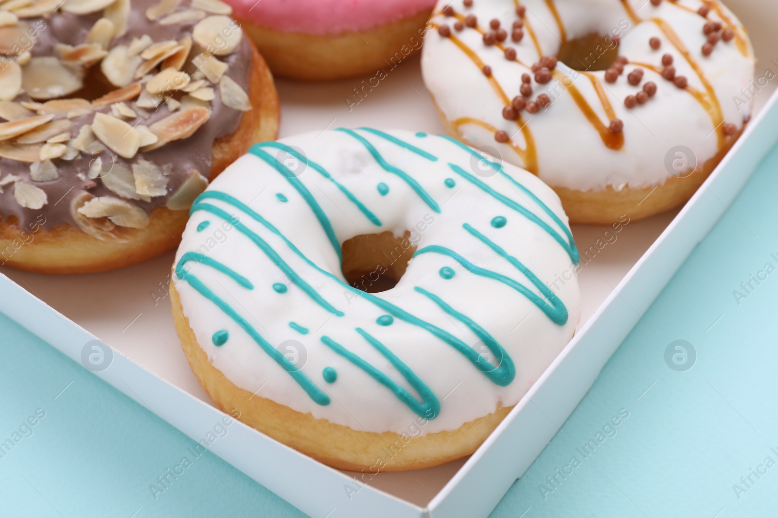 Photo of Box with different tasty glazed donuts on light blue background, closeup