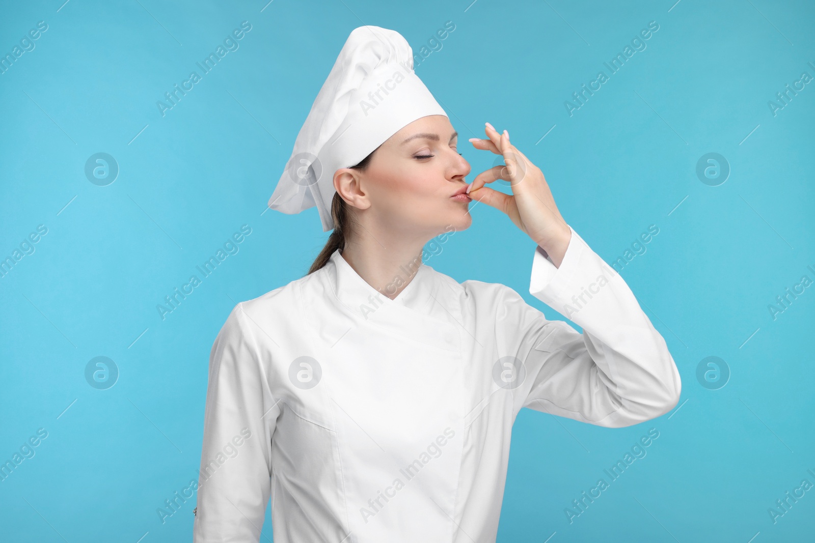 Photo of Woman chef in uniform showing perfect sign on light blue background