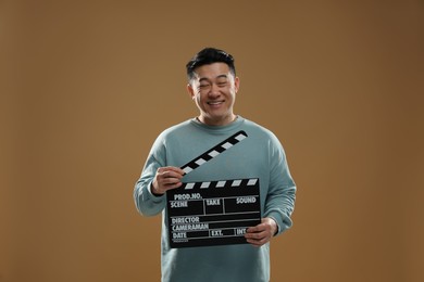 Happy asian actor with clapperboard on brown background. Film industry