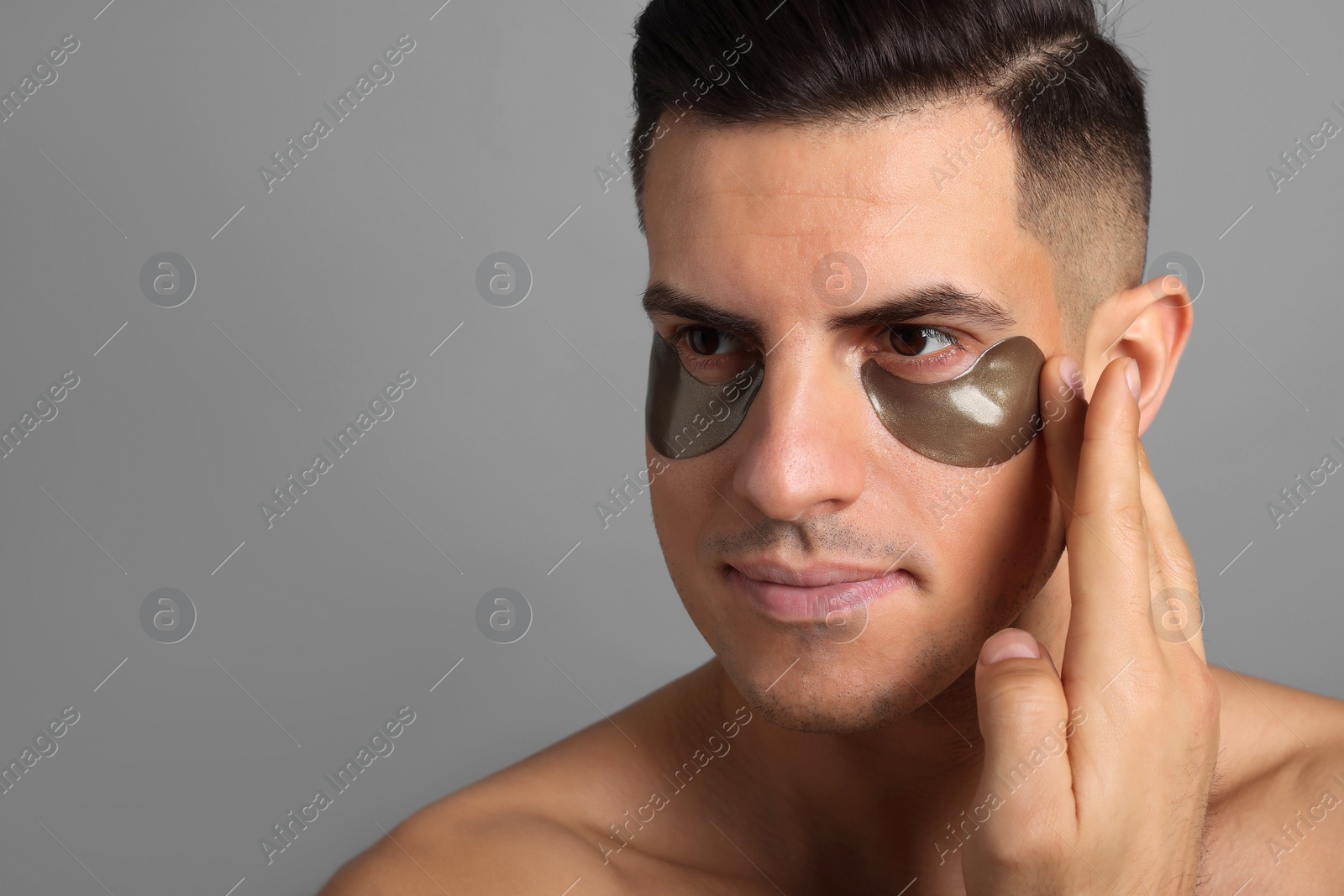 Photo of Man applying dark under eye patch on grey background. Space for text