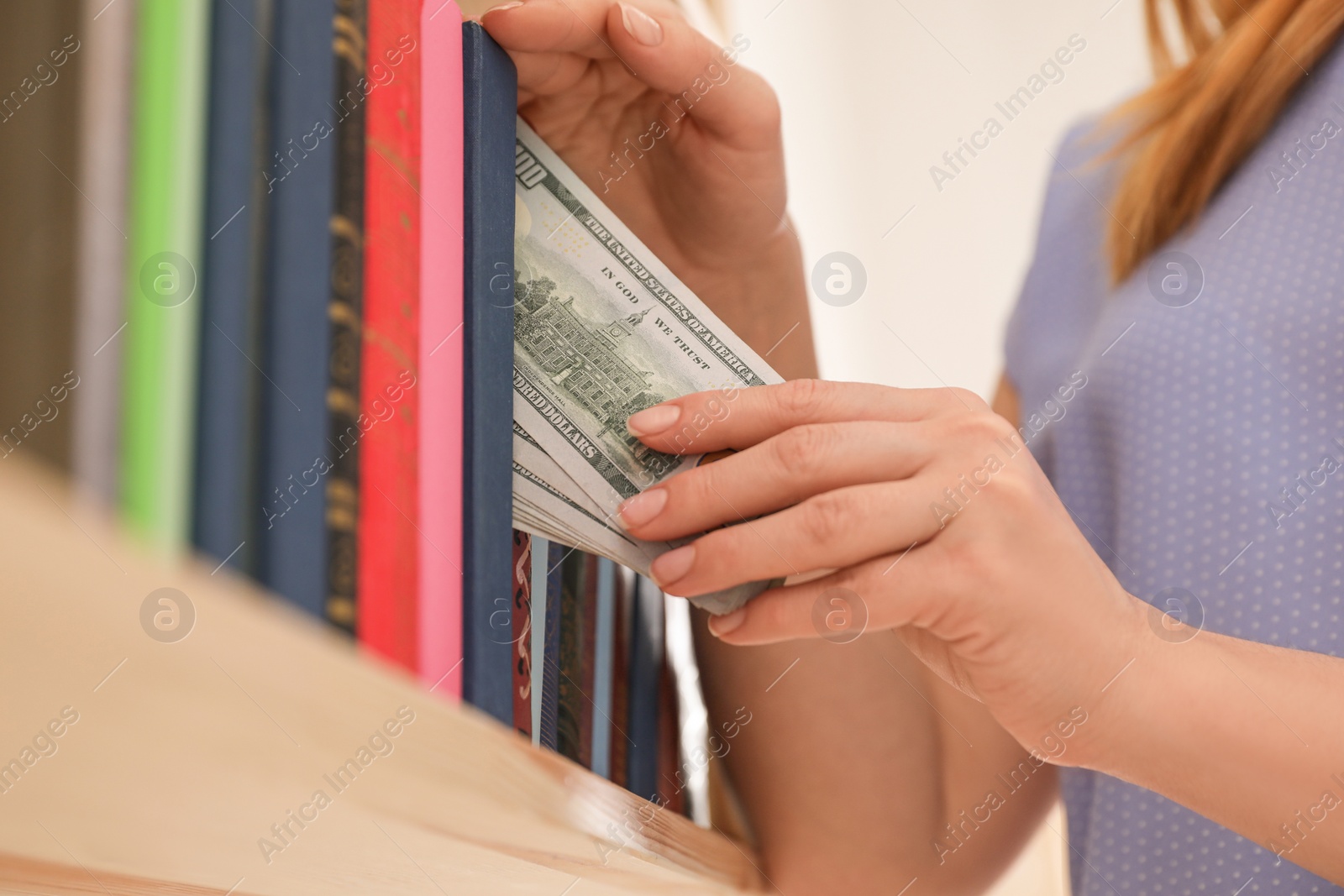 Photo of Woman hiding money between books on shelf indoors, closeup. Financial savings