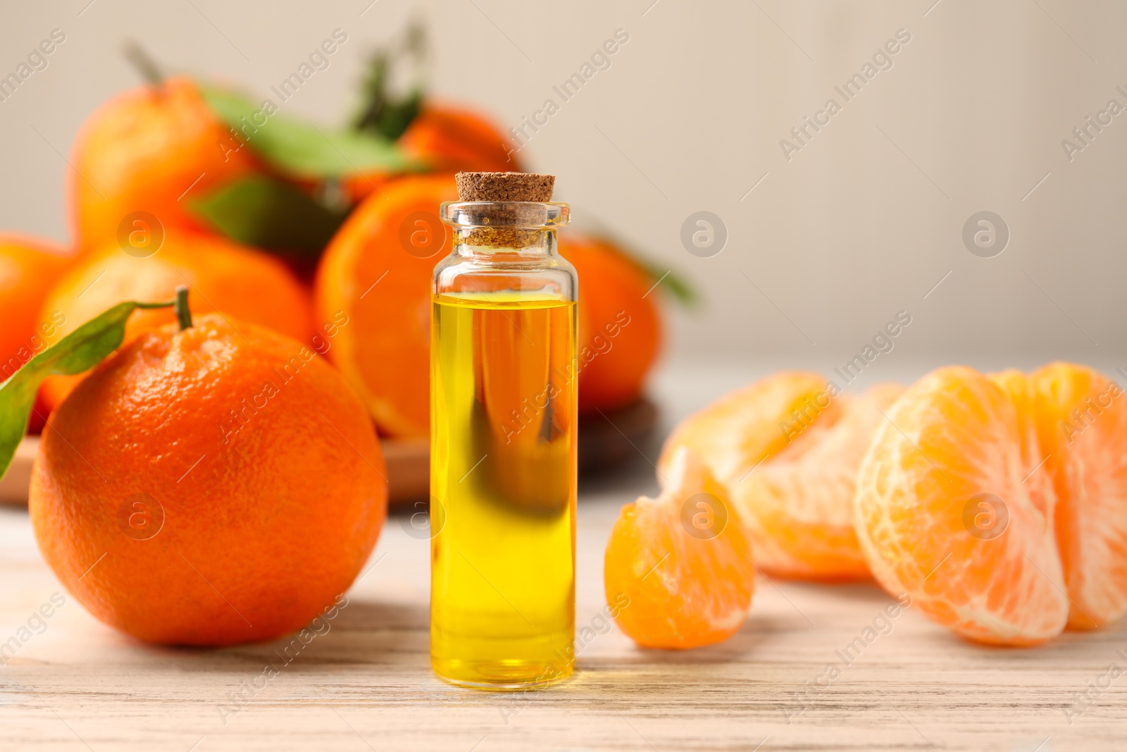 Photo of Bottle of tangerine essential oil and fresh fruits on white wooden table, closeup