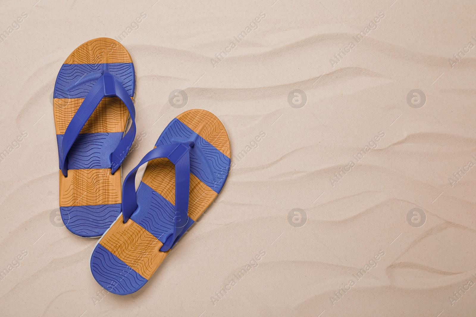 Photo of Pair of striped flip flops on sand, flat lay. Space for text