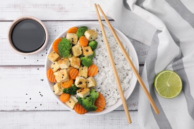 Photo of Delicious rice with fried tofu, broccoli and carrots served on white wooden table, flat lay