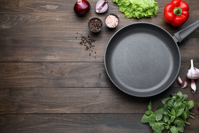 Empty frying pan, fresh vegetables and spices on wooden table, flat lay. Space for text