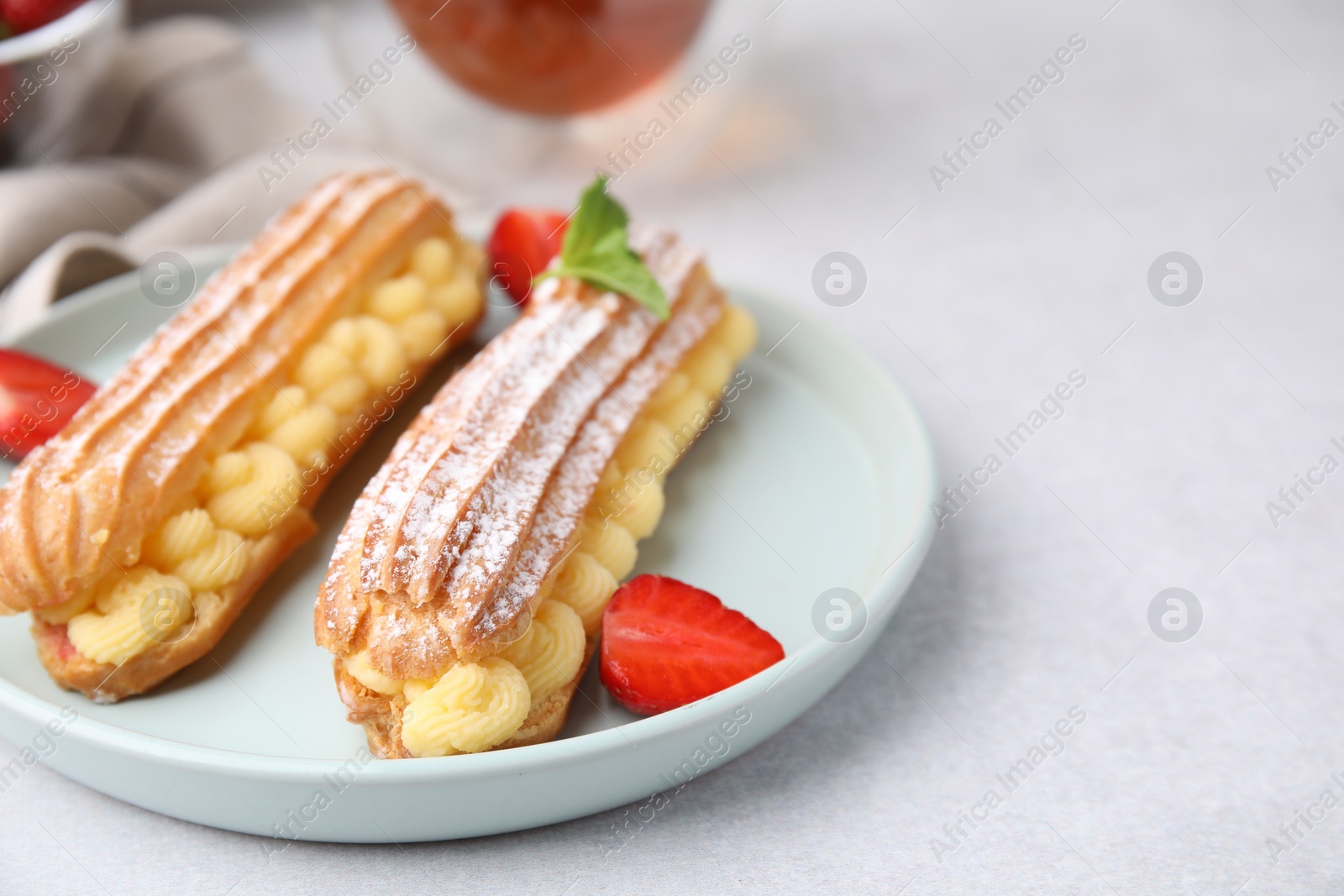 Photo of Delicious eclairs filled with cream, strawberries and mint on light table, closeup. Space for text