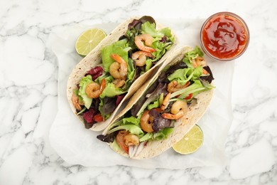 Delicious tacos with shrimps, lime and sauce on white marble table, flat lay