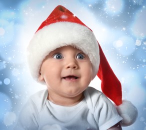 Cute baby in Santa hat against blurred lights. Christmas celebration