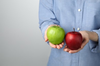 Photo of Woman holding fresh ripe red and green apples on grey background, closeup. Space for text