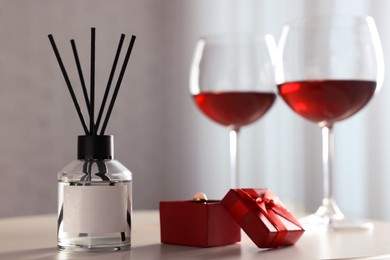 Reed diffuser, glasses of wine and gift box on white table indoors