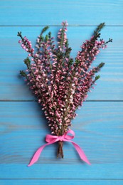 Photo of Bunch of heather branches with beautiful flowers and ribbon on light blue wooden table, top view