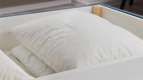 Storage drawer under bed with white pillows indoors, closeup