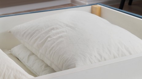 Photo of Storage drawer under bed with white pillows indoors, closeup