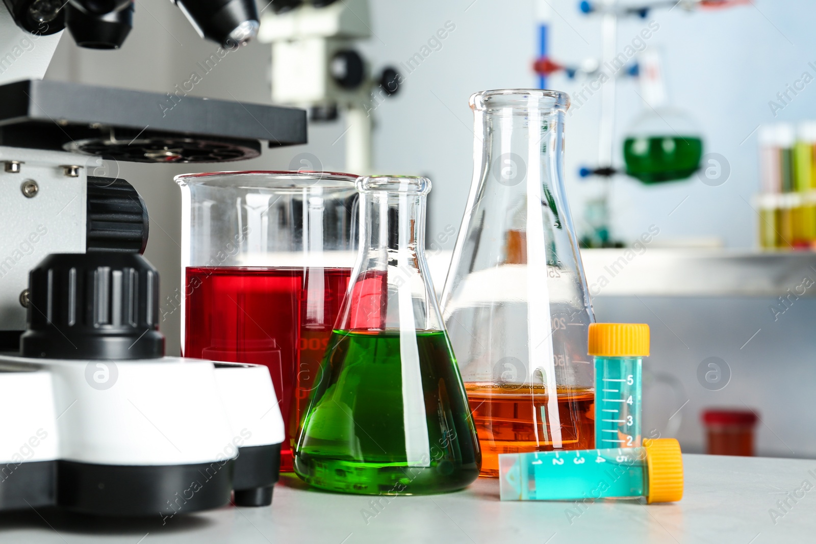 Photo of Different glassware with samples and microscope on table in chemistry laboratory