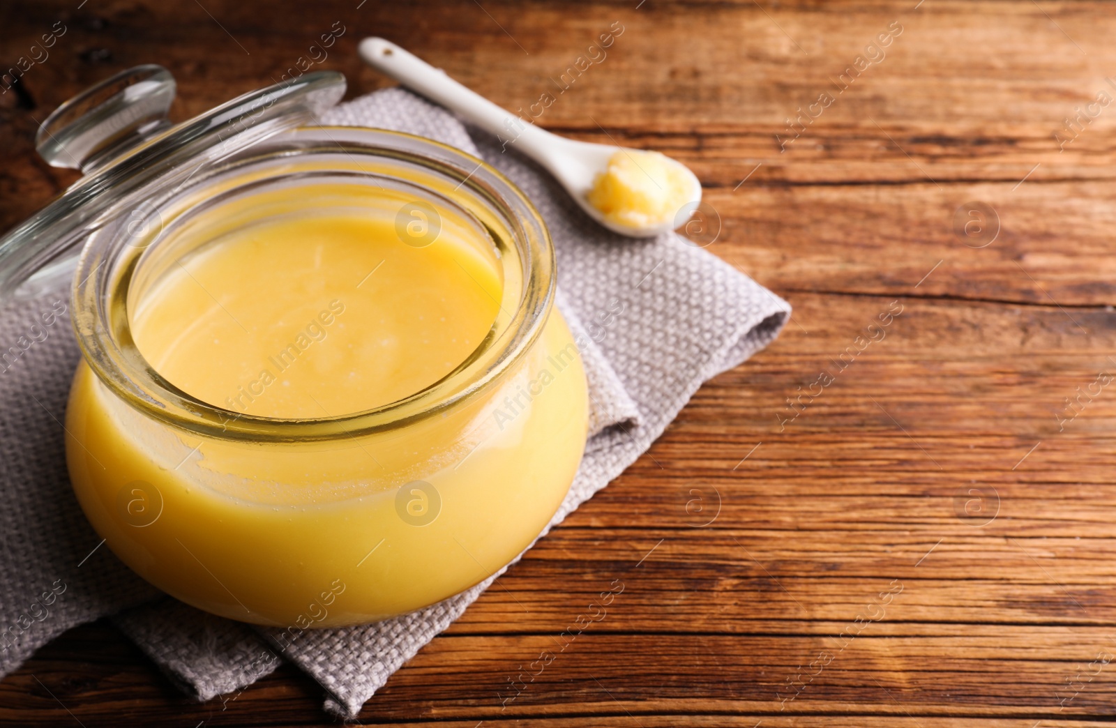 Photo of Glass jar and spoon of Ghee butter on wooden table, closeup. Space for text