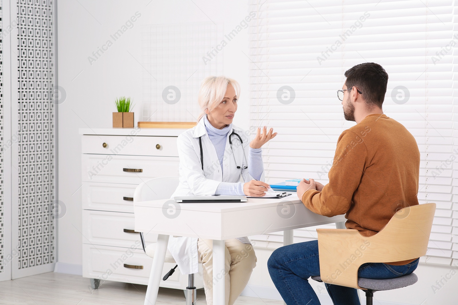 Photo of Doctor consulting patient at white table in clinic