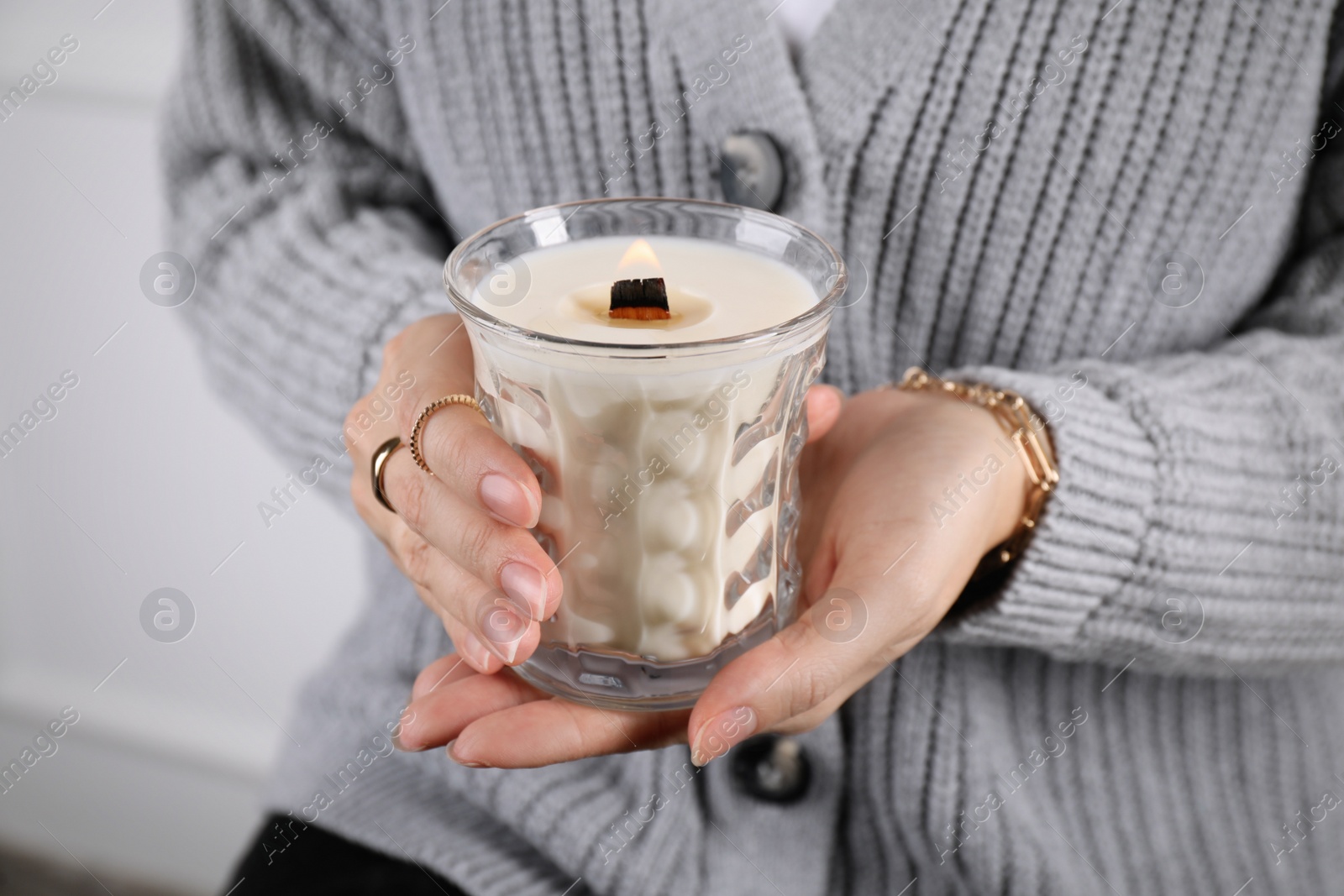 Photo of Woman with stylish jewelry holding burning soy candle on light background, closeup