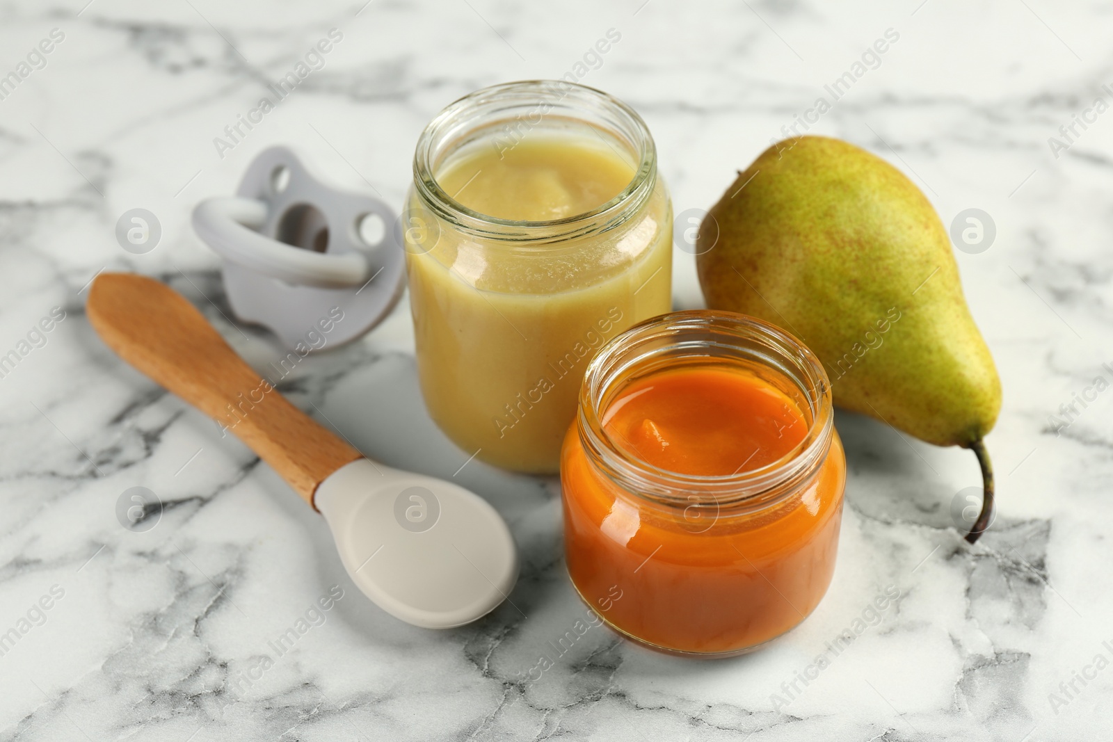 Photo of Tasty baby food in jars, pear and spoon on white marble table
