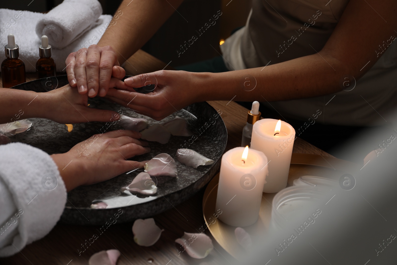 Photo of Woman receiving hand massage in spa salon, closeup. Bowl of water and flower petals on table