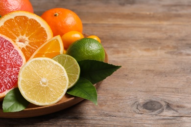 Photo of Fresh juicy citrus fruits with green leaves on wooden table. Space for text