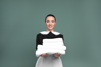 Young chambermaid with stack of clean towels on color background