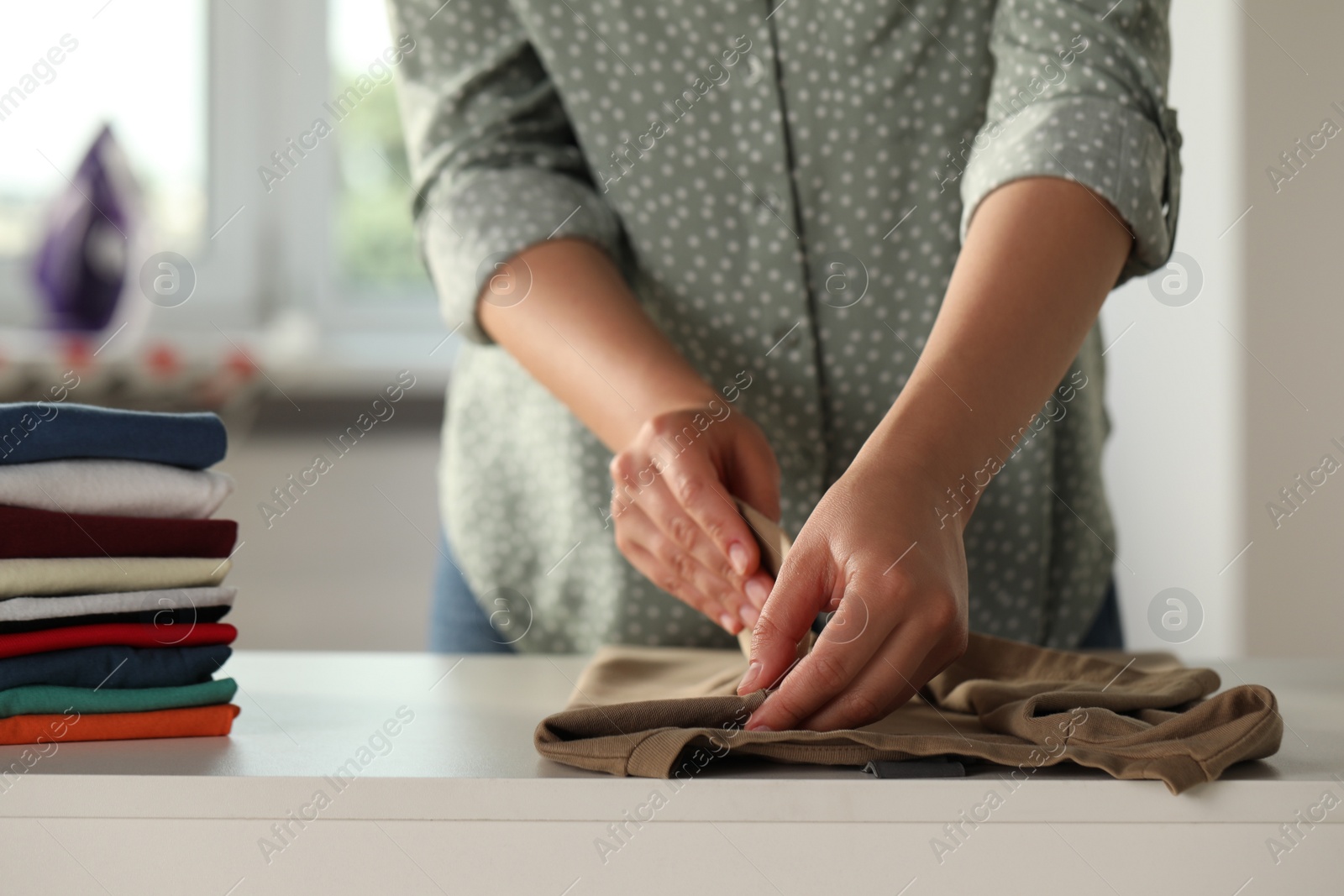 Photo of Woman folding clothes at white table indoors, closeup