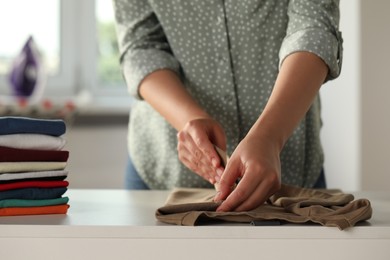 Photo of Woman folding clothes at white table indoors, closeup