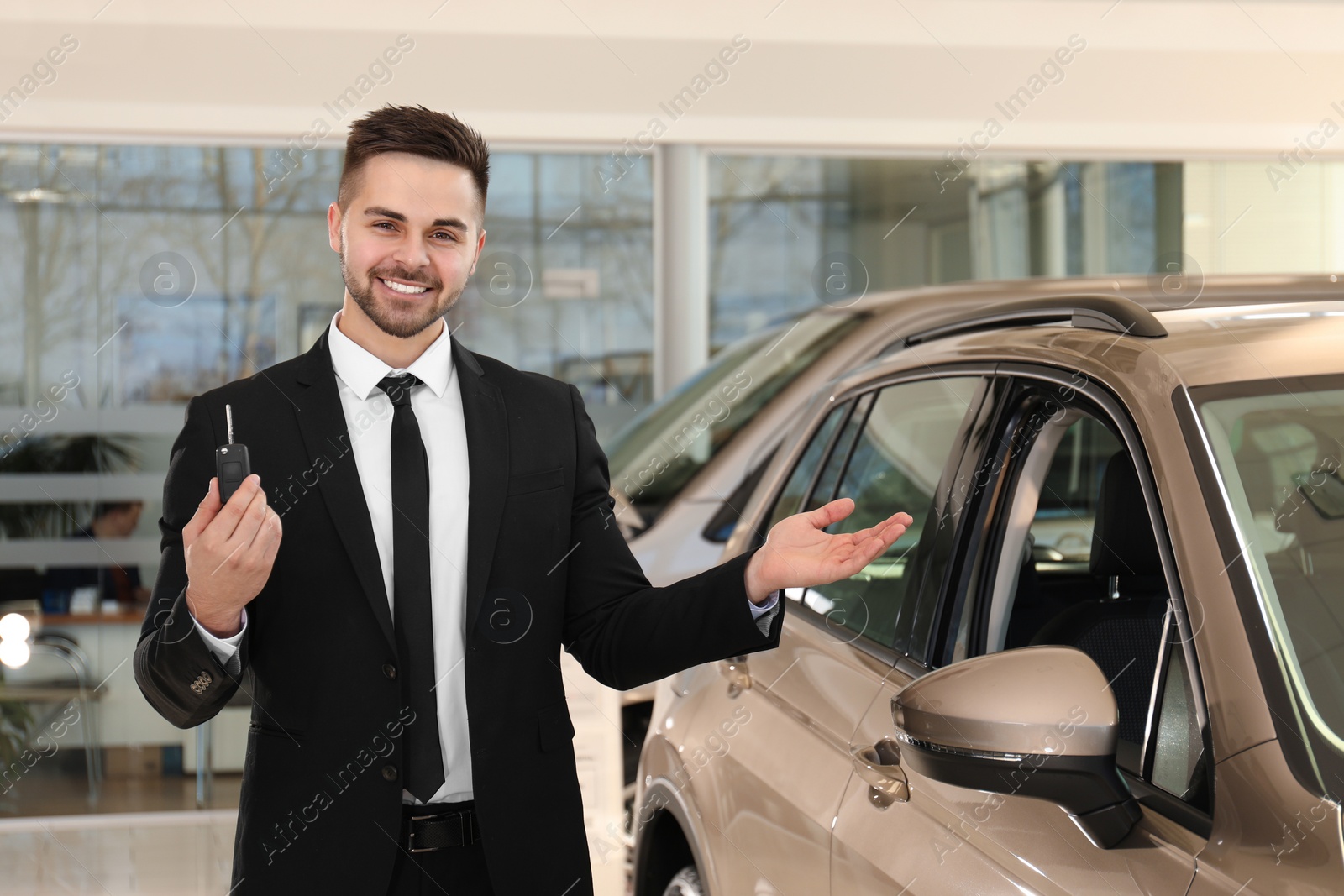 Photo of Young salesman with key near car in dealership