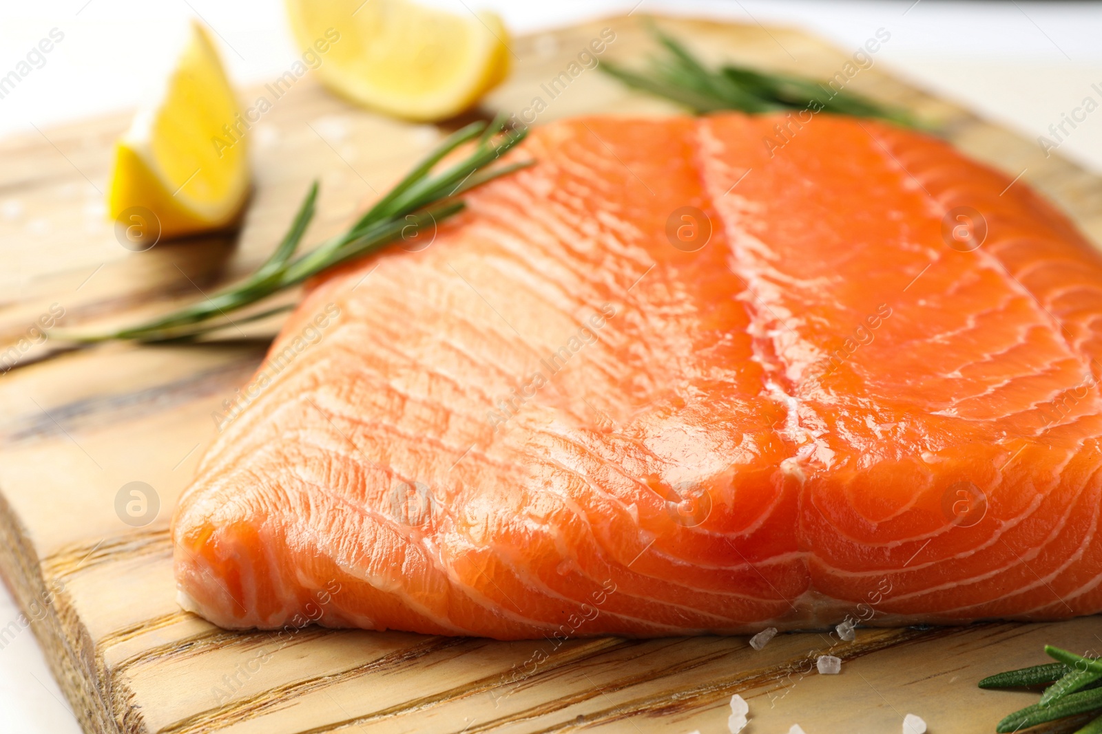 Photo of Fresh salmon fillet with rosemary and salt on wooden board, closeup