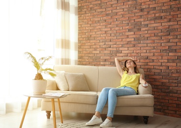 Woman with air conditioner remote suffering from heat at home