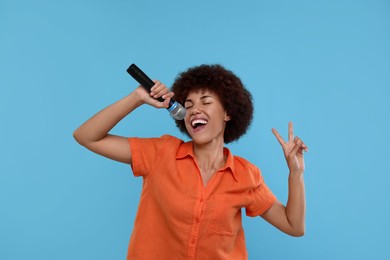 Photo of Curly young woman with microphone singing and showing victory sign on light blue background