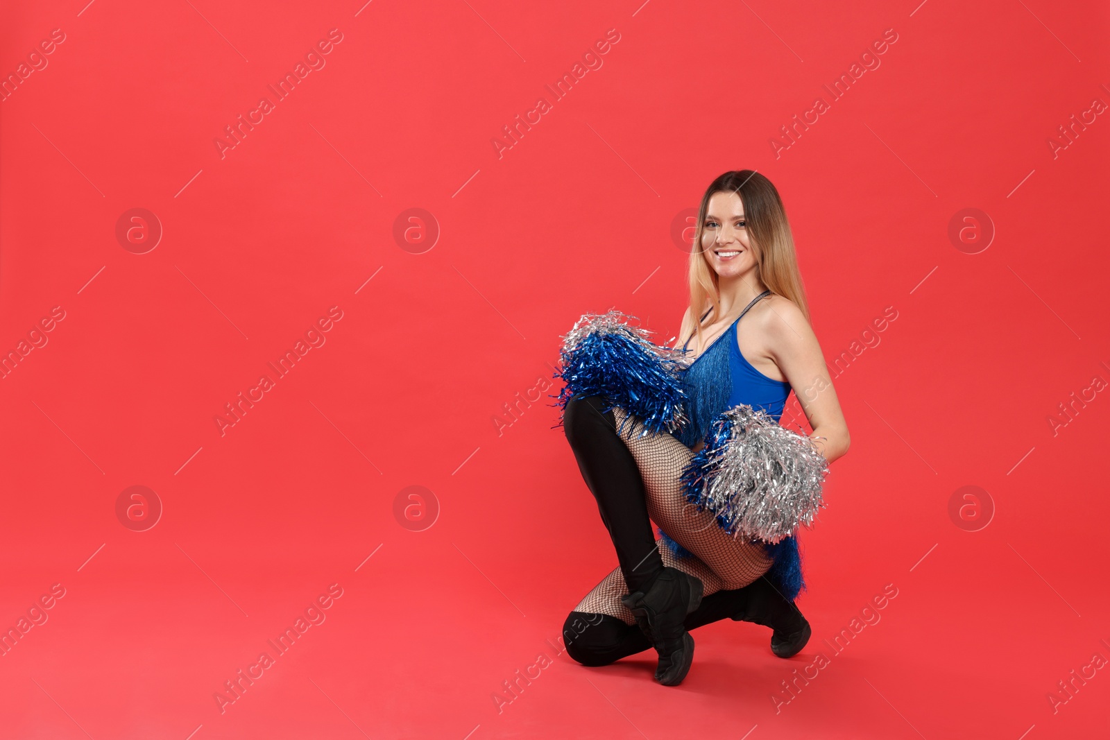 Photo of Beautiful cheerleader in costume holding pom poms on red background. Space for text