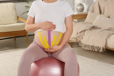 Photo of Pregnant woman with kinesio tapes doing exercises on fitball at home, closeup