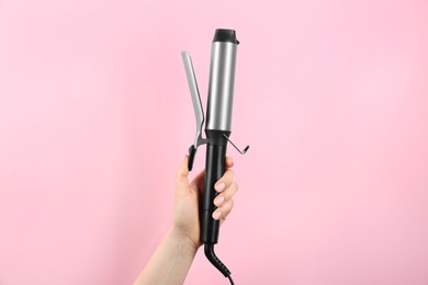 Photo of Hair styling appliance. Woman holding curling iron on pink background, closeup