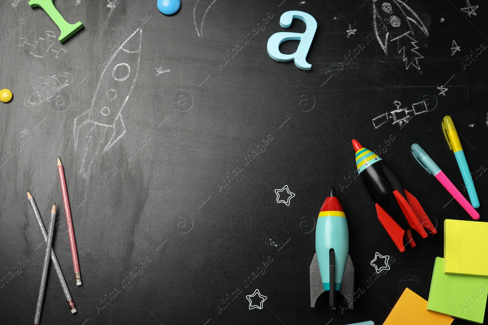 Photo of Bright toy rockets, school supplies and drawings on chalkboard, flat lay. Space for text
