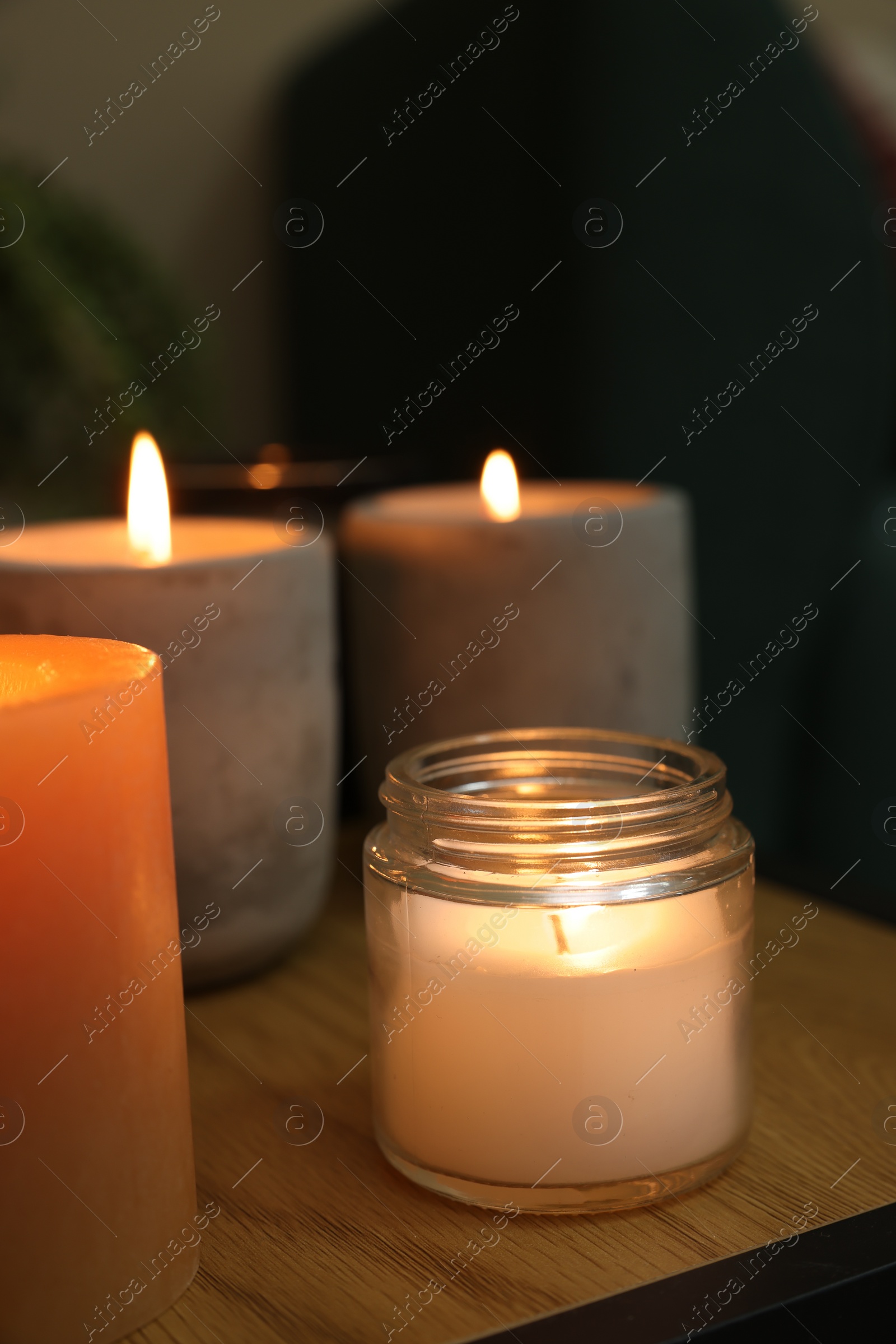 Photo of Lit candles in different holders on wooden table indoors