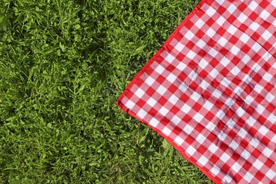 Photo of Checkered picnic tablecloth on fresh green grass, top view. Space for text