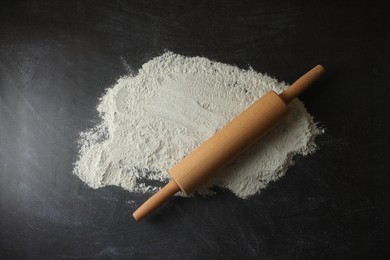 Photo of Flour and rolling pin on black table, top view