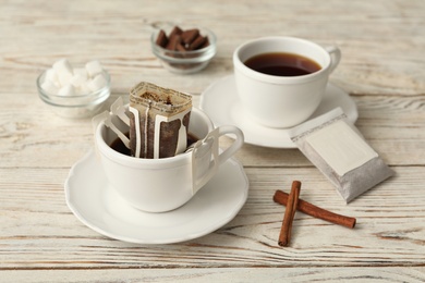 Photo of Cup with drip coffee bag and cinnamon on white wooden table