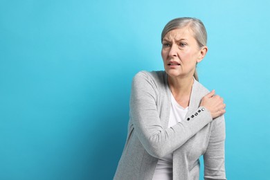 Arthritis symptoms. Woman suffering from pain in shoulder on light blue background, space for text