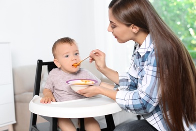 Photo of Woman feeding her child in highchair indoors. Healthy baby food