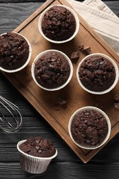 Delicious chocolate muffins on black wooden table, flat lay