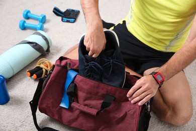 Photo of Man packing sports stuff for training into bag on floor indoors, closeup