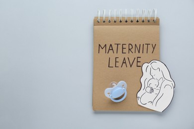 Photo of Maternity leave concept. Notebook, baby pacifier, paper cutout of mother and child on light grey background, top view. Space for text