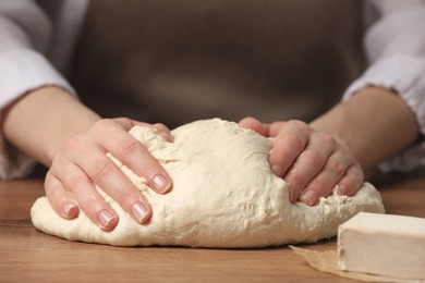 Photo of Woman kneading yeast dough for cake at wooden table, closeup