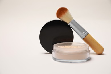 Photo of Loose face powder and makeup brush on light background, closeup