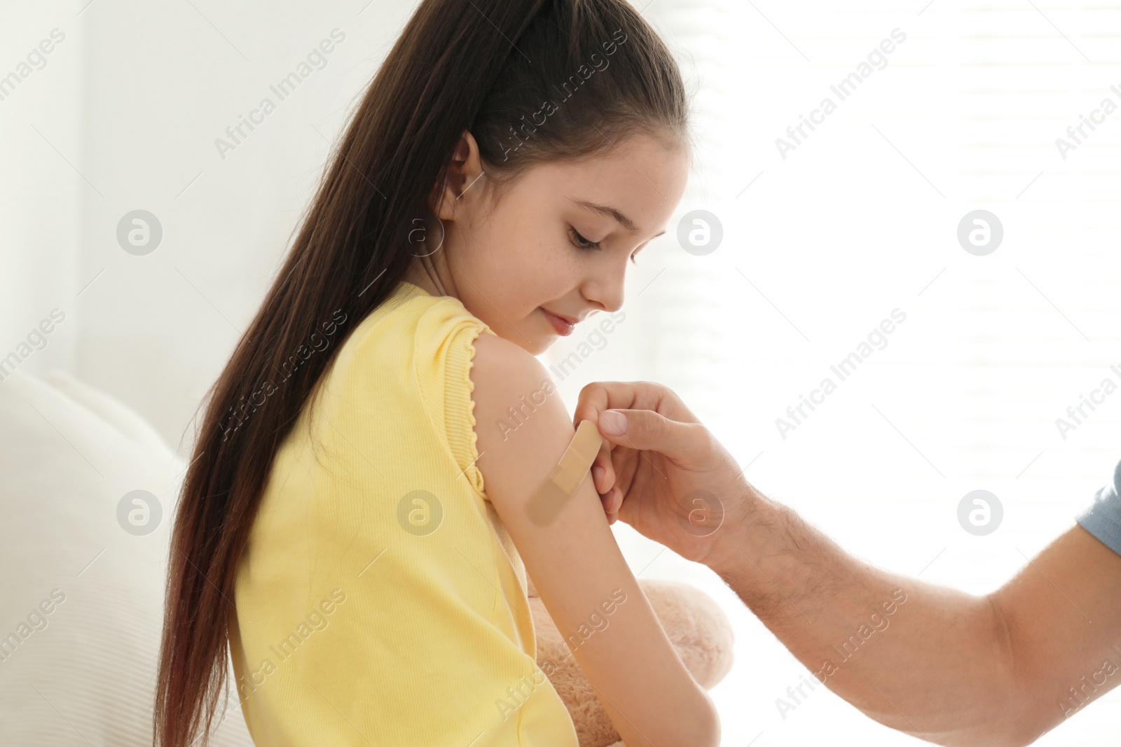 Photo of Father putting sticking plaster onto daughter's arm at home