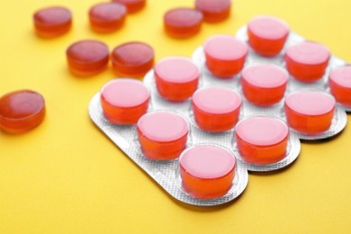 Blister with orange cough drops on yellow background, closeup