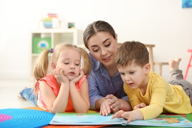 Photo of Kindergarten teacher reading book to children indoors. Learning and playing