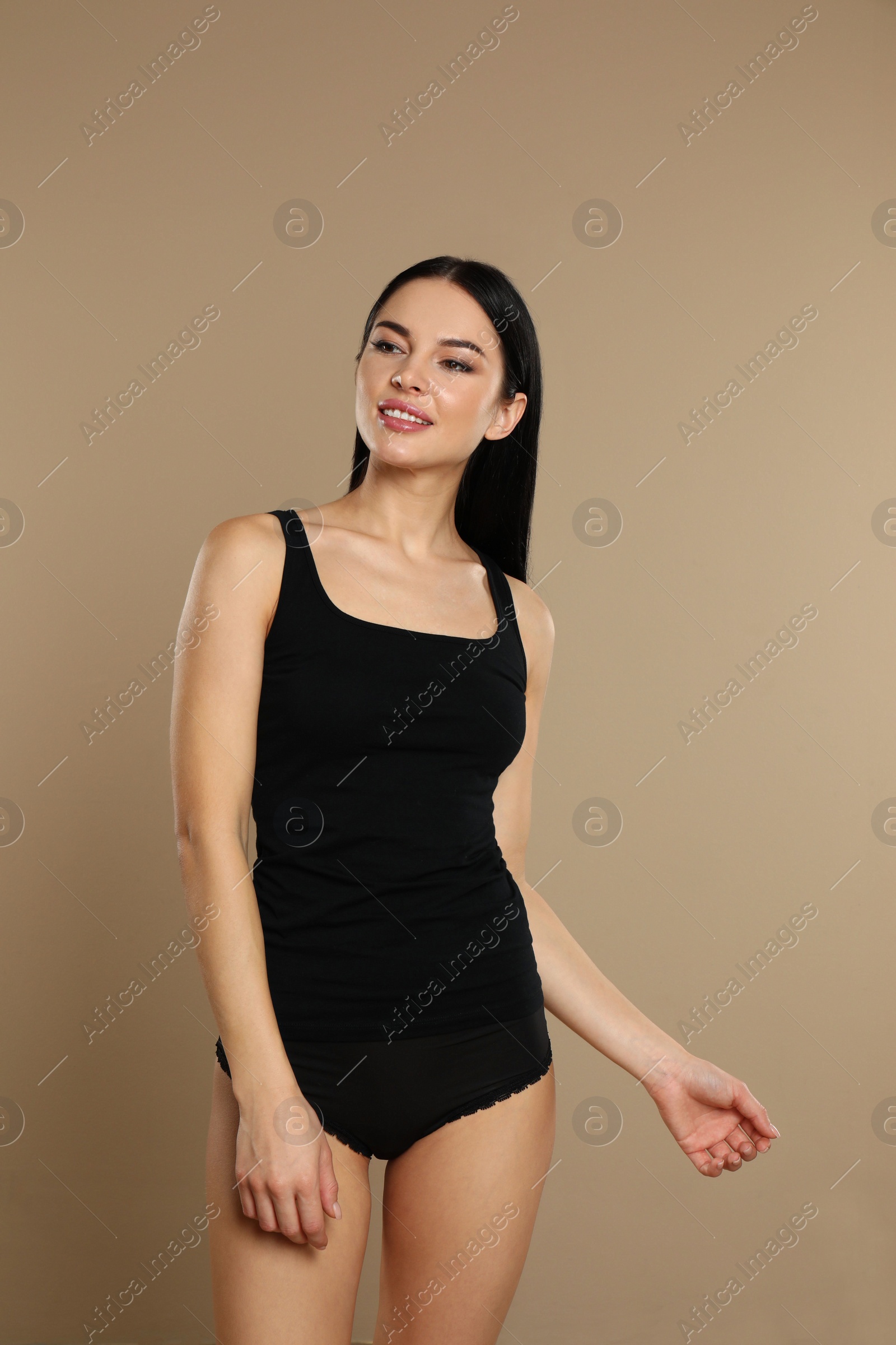 Photo of Beautiful young woman in black underwear on beige background